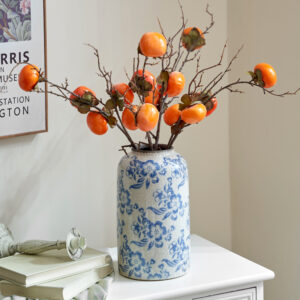 Grand vase en porcelaine floral bleu et blanc tenant des branches de kaki orange sur une armoire blanche.