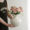 Person placing pink roses in classic ribbed white ceramic vase on neutral background